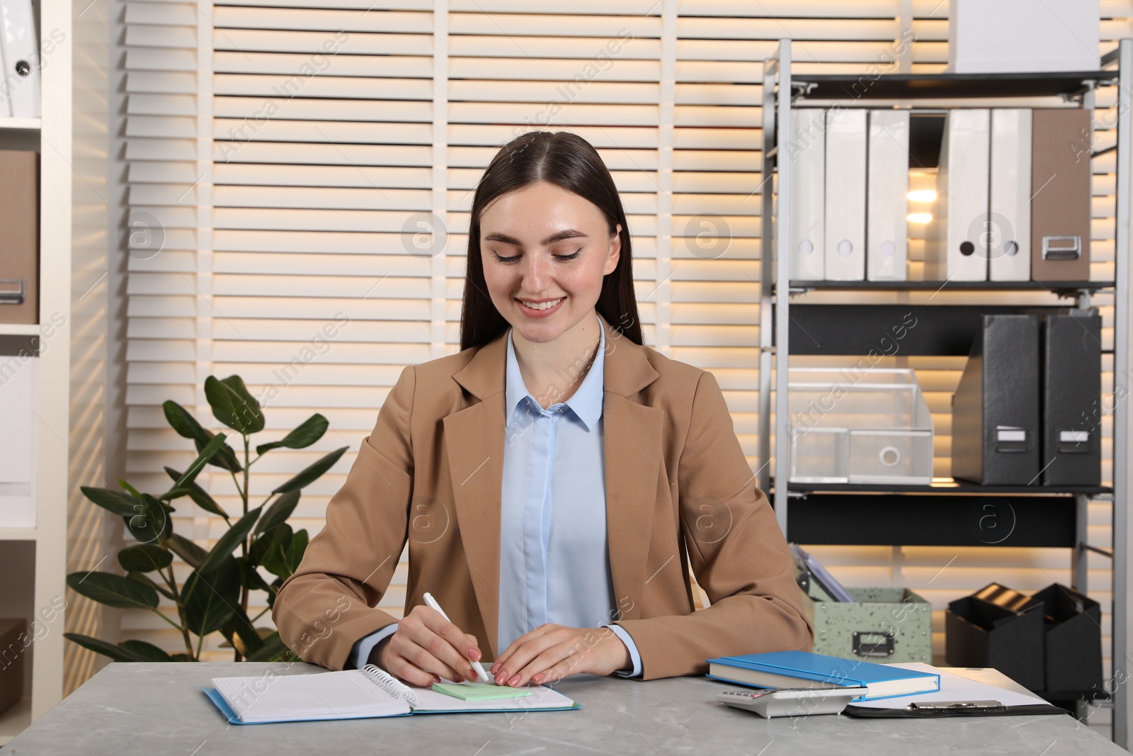 Photo of Happy woman taking notes at light grey marble table in office