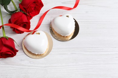 St. Valentine's Day. Delicious heart shaped cakes and roses on white wooden table, flat lay. Space for text