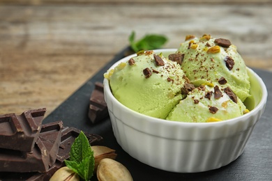 Photo of Delicious green ice cream served in ceramic bowl on wooden table