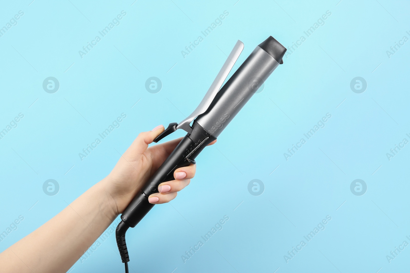 Photo of Hair styling appliance. Woman holding curling iron on light blue background, closeup