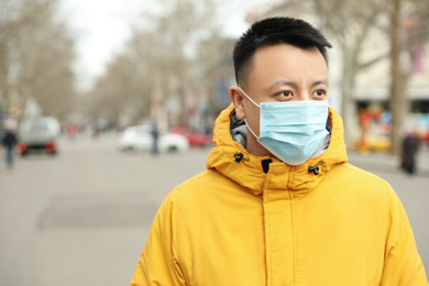 Photo of Asian man wearing medical mask on city street, space for text. Virus outbreak