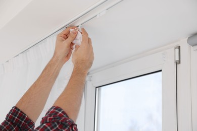 Photo of Worker hanging window curtain indoors, closeup view