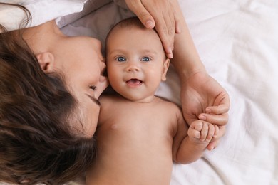 Photo of Young mother with her cute baby on bed, top view