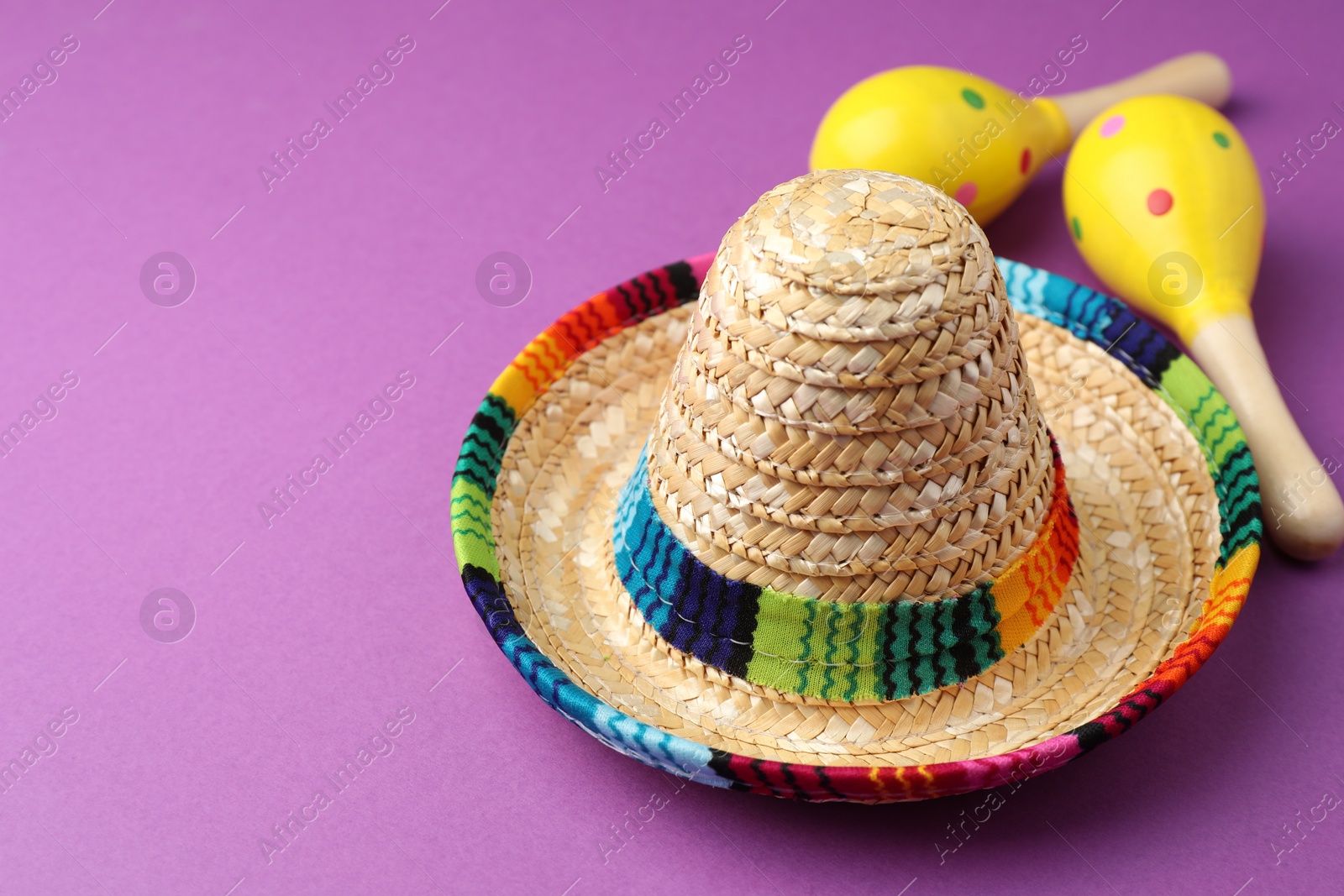 Photo of Mexican sombrero hat and maracas on purple background. Space for text