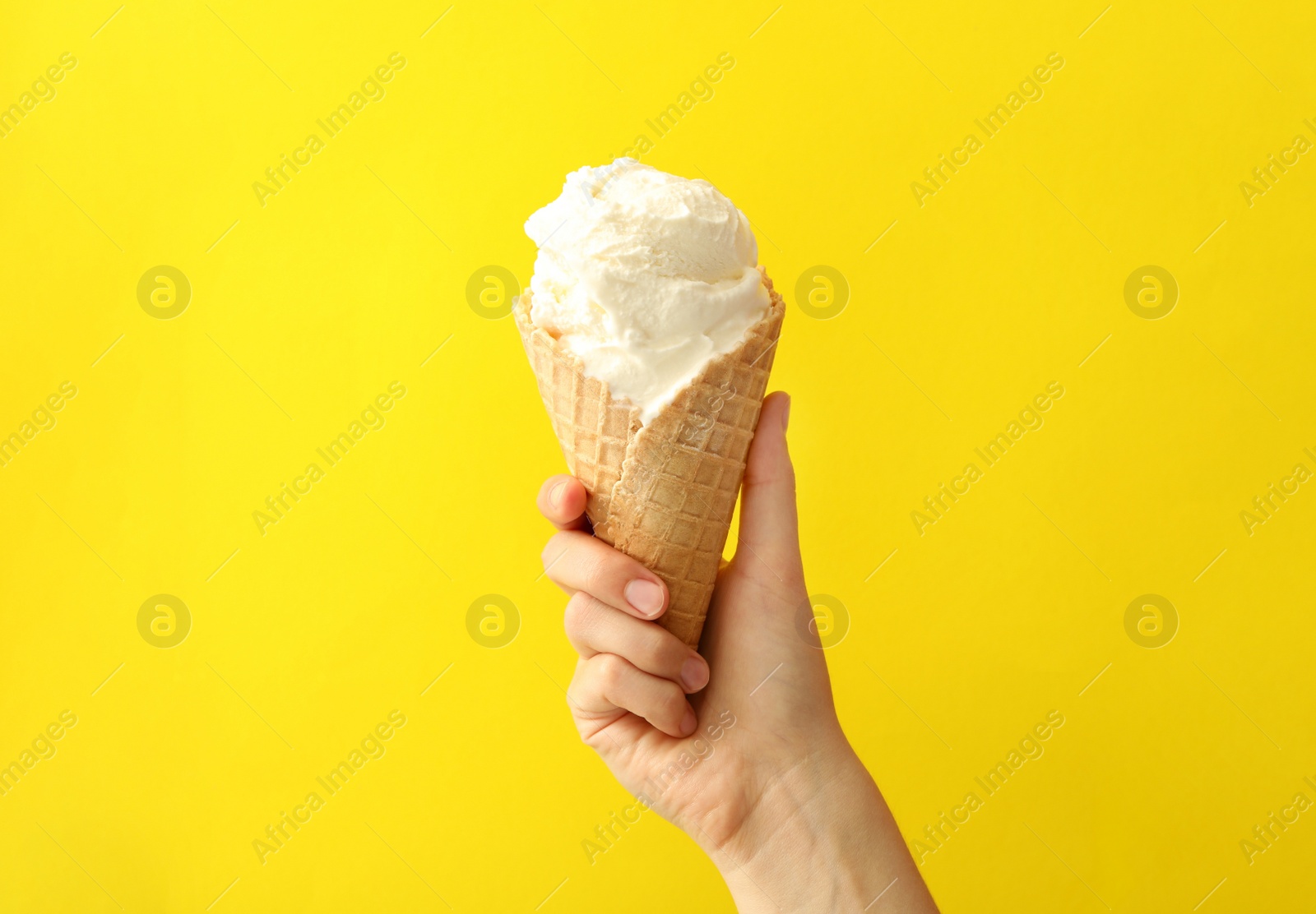 Photo of Woman holding waffle cone with delicious ice cream on yellow background, closeup