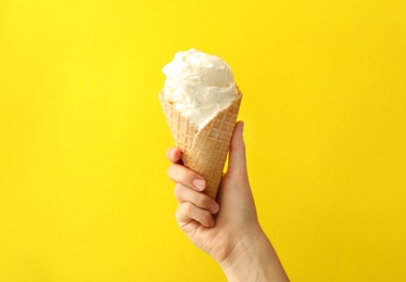 Woman holding waffle cone with delicious ice cream on yellow background, closeup