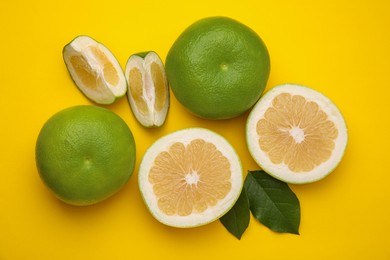 Photo of Whole and cut sweetie fruits with green leaves on yellow background, flat lay