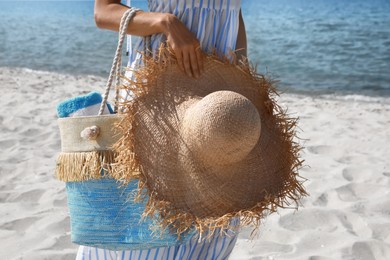 Photo of Woman with beach bag and straw hat near sea on sunny day, closeup