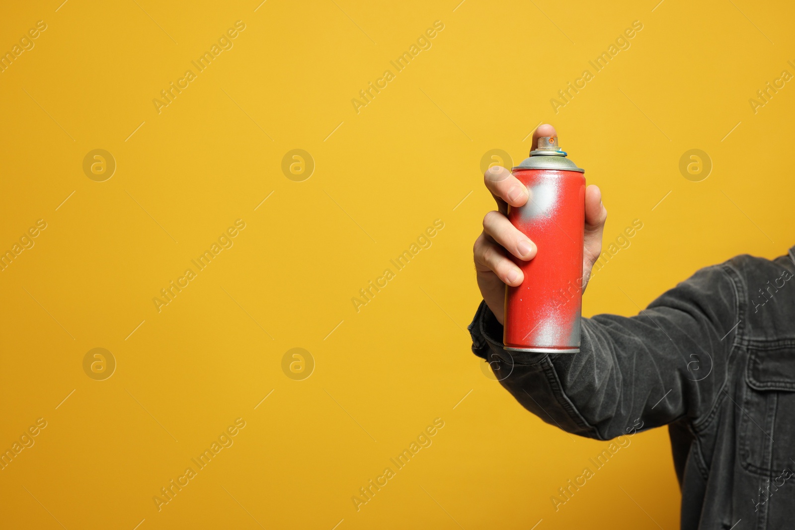 Photo of Man holding can of spray paint on yellow background, closeup. Space for text