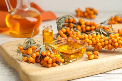 Natural sea buckthorn oil and fresh berries on white wooden table