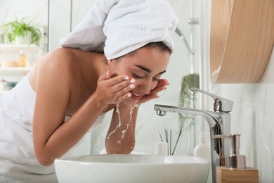 Photo of Beautiful young woman washing her face with water in bathroom