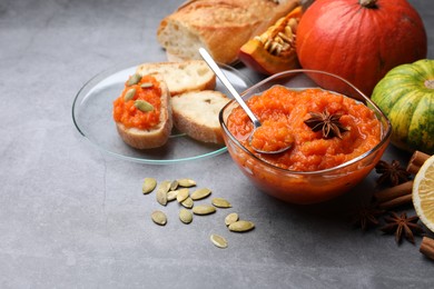 Photo of Delicious pumpkin jam and ingredients on grey table, space for text