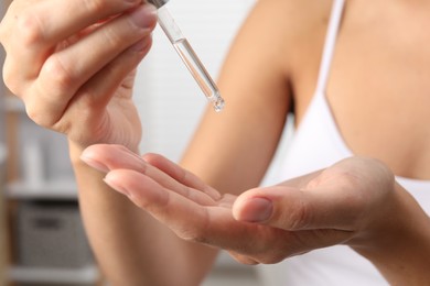 Woman applying cosmetic serum onto her hand on blurred background, closeup