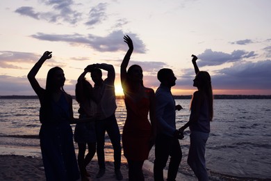 Image of Friends dancing at sunset during summer party. Silhouettes of people near river