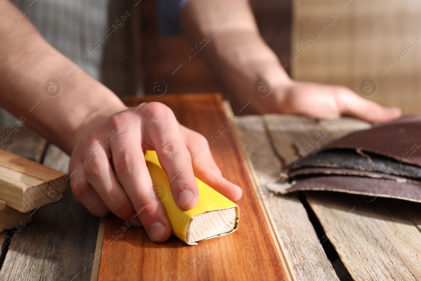 Photo of Man polishing wooden plank with sandpaper at table indoors, closeup