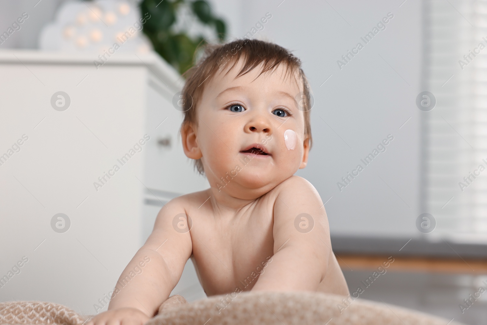 Photo of Cute little baby with moisturizing cream on face indoors