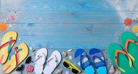 Many different flip flops and sunglasses on light blue wooden background, flat lay. Space for text