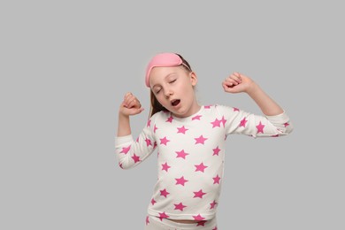 Girl with sleep mask yawning on light grey background. Insomnia problem