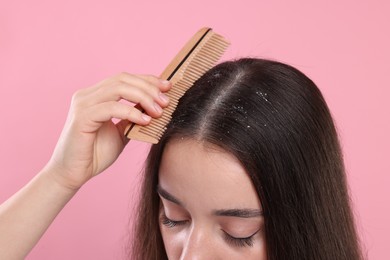 Photo of Woman with comb examining her hair and scalp on pink background, closeup. Dandruff problem