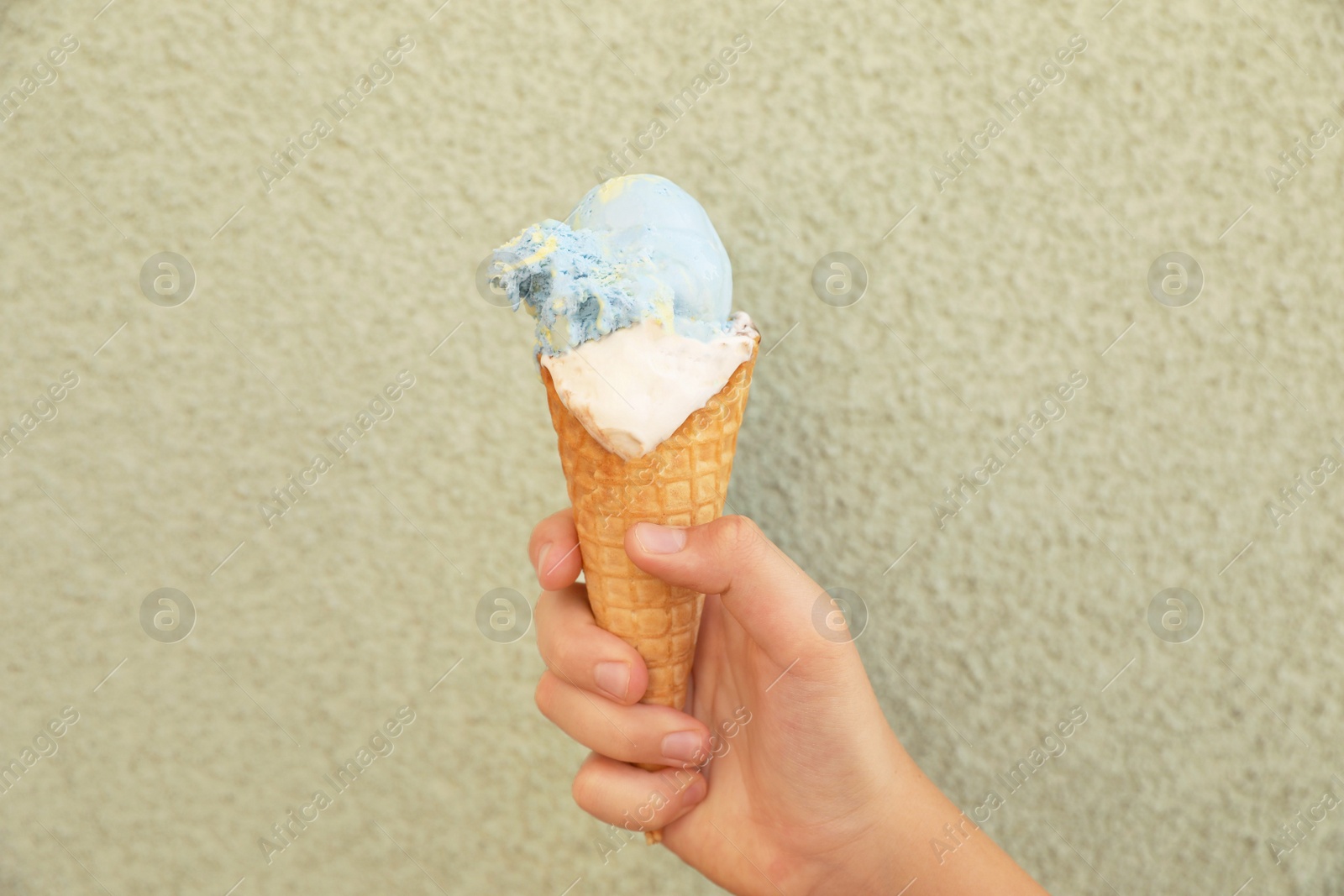 Photo of Woman holding delicious ice cream in wafer cone near wall outdoors, closeup