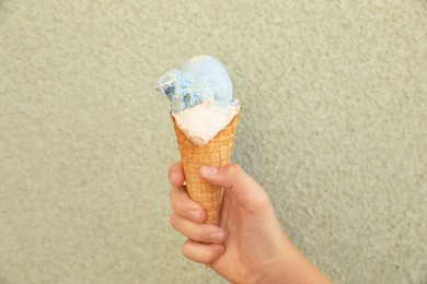 Woman holding delicious ice cream in wafer cone near wall outdoors, closeup