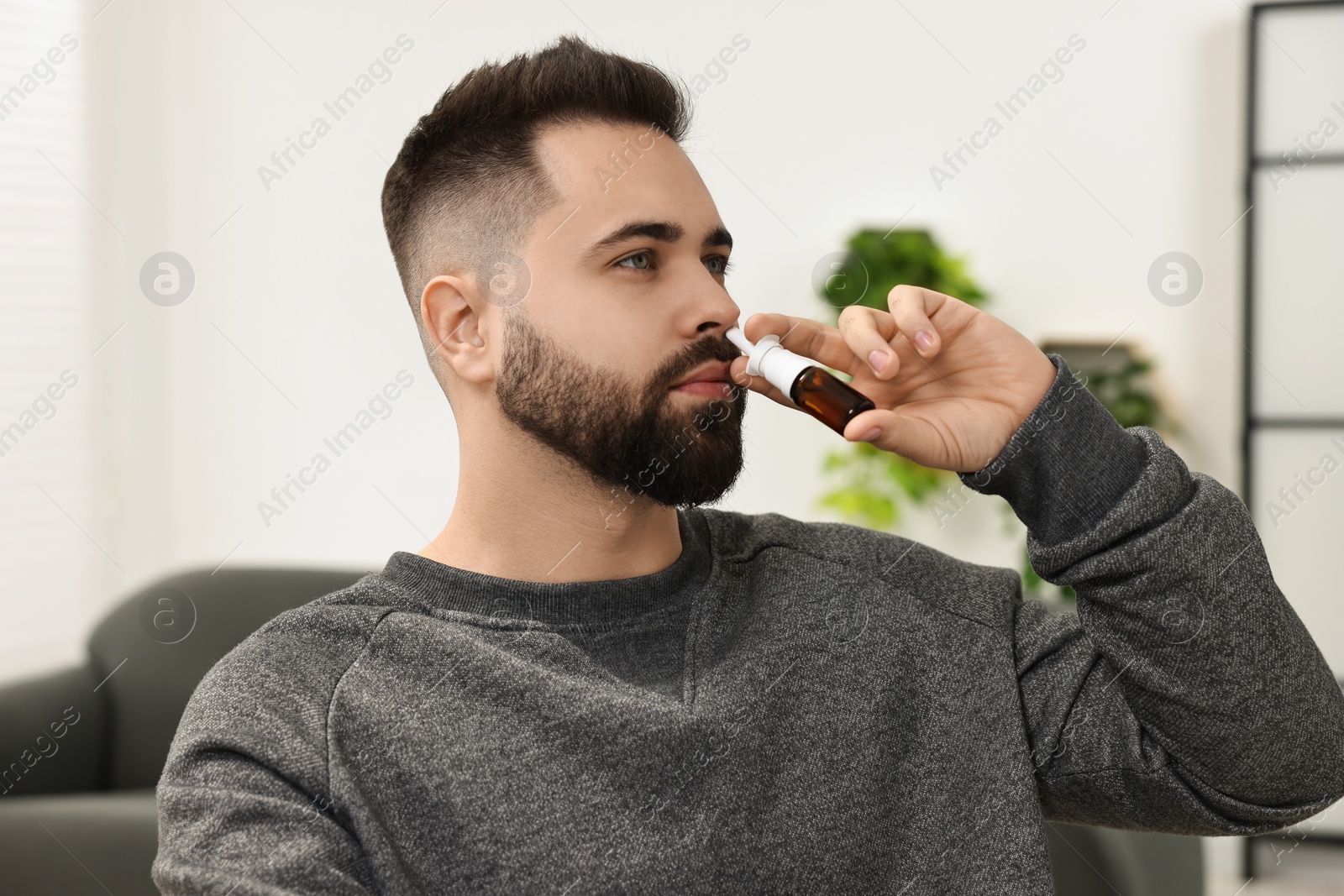 Photo of Medical drops. Young man using nasal spray indoors