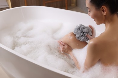 Photo of Woman taking bath with mesh pouf in tub, closeup