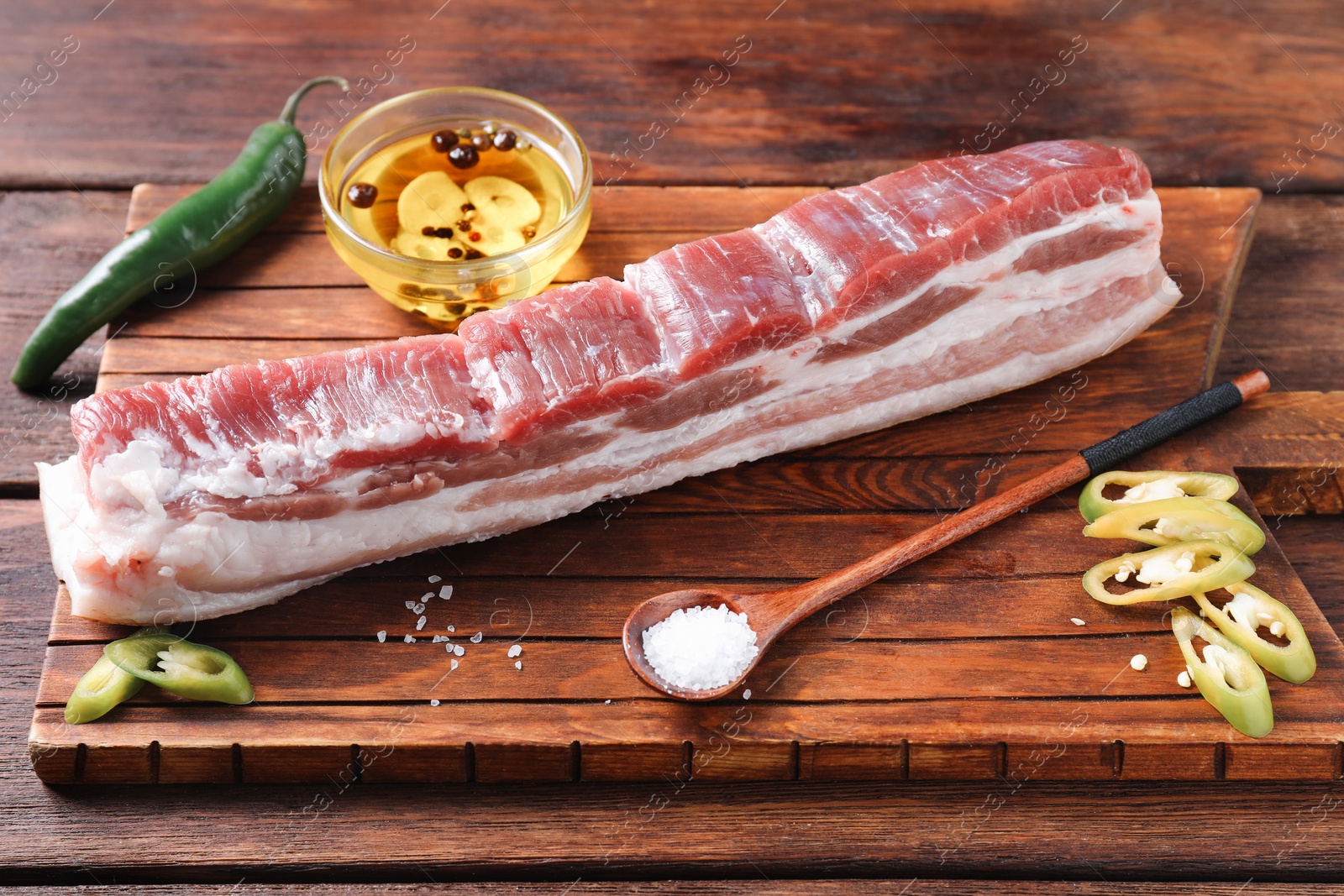 Photo of Piece of raw pork belly, green chili pepper and oil with spices on wooden table