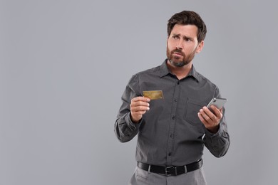 Emotional man with smartphone and credit card on light grey background, space for text. Be careful - fraud