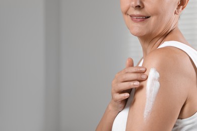 Photo of Happy woman applying body cream onto arm indoors, closeup. Space for text