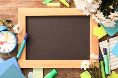 Photo of Blackboard, stationery, alarm clock and flowers on wooden table, flat lay with space for text. Teacher's Day