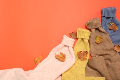 Photo of Warm sweaters and dry leaves on orange background, flat lay with space for text. Autumn season