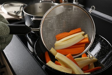 Woman putting cut parsnips and carrots into wok pan in kitchen, closeup