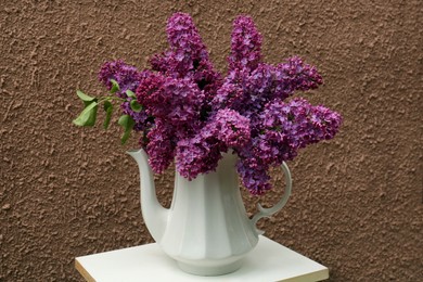 Photo of Beautiful lilac flowers in teapot near brown wall