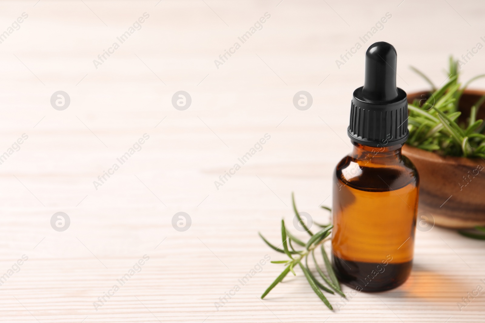 Photo of Bottle with essential oil and fresh rosemary on white wooden table, space for text