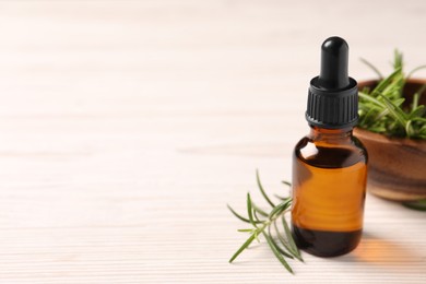 Bottle with essential oil and fresh rosemary on white wooden table, space for text