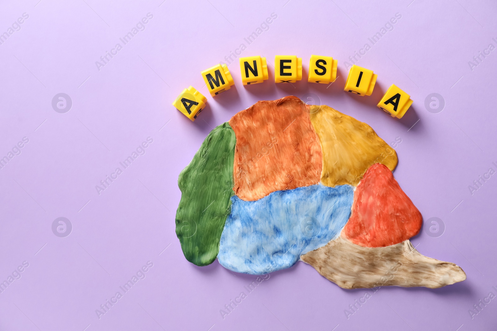 Photo of Word Amnesia made of yellow cubes and brain with sections on violet background, flat lay. Space for text