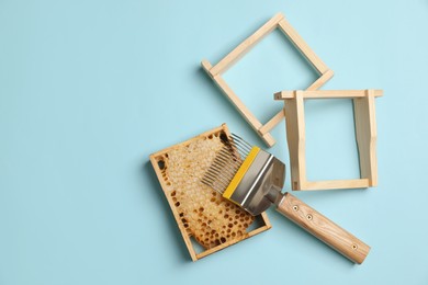Photo of Honeycomb, frames and uncapping fork on light blue background, flat lay with space for text. Beekeeping