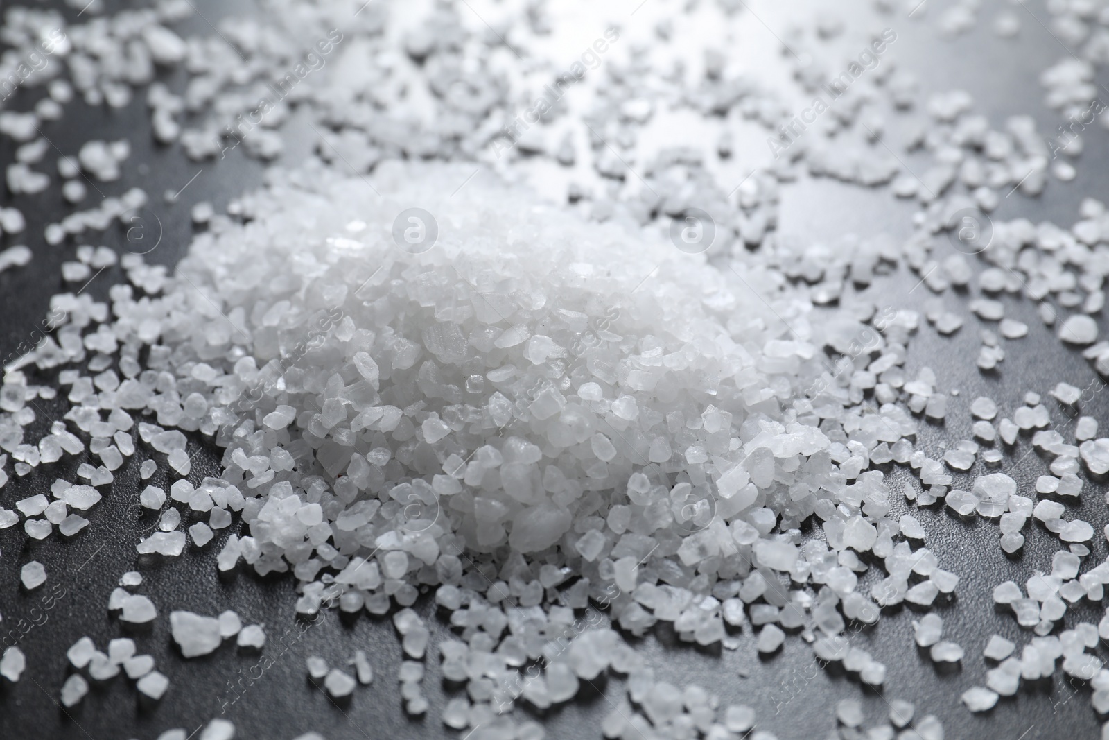 Photo of Heap of natural salt on black table, closeup