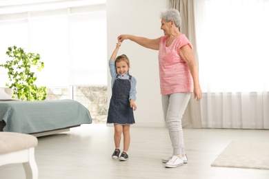 Photo of Cute girl and her grandmother dancing at home