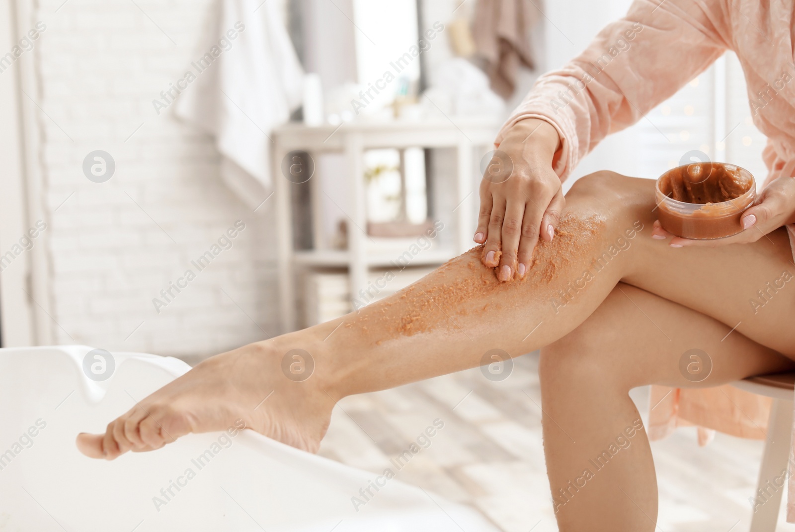 Photo of Young woman applying natural scrub onto her skin in bathroom