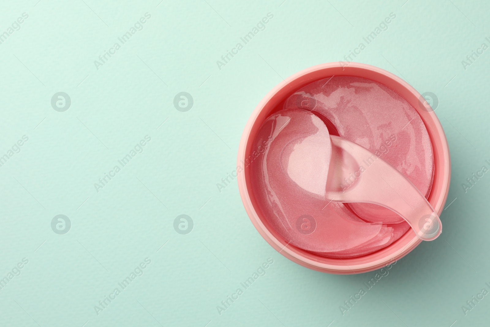 Photo of Jar of under eye patches and spoon on turquoise background, top view with space for text. Cosmetic product