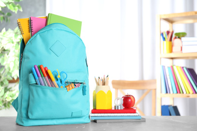 Stylish backpack with different school stationery on table indoors. Space for text