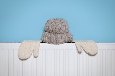 Photo of Modern radiator with knitted hat and mittens near light blue wall indoors