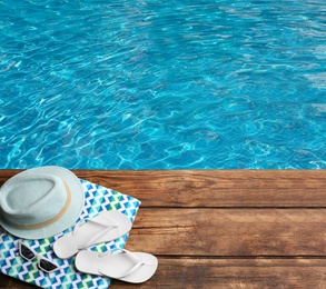 Image of Beach accessories on wooden deck near swimming pool, flat lay. Space for text 