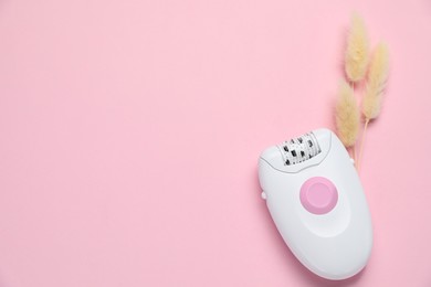 Modern epilator and fluffy dry plants on pink background, flat lay. Space for text