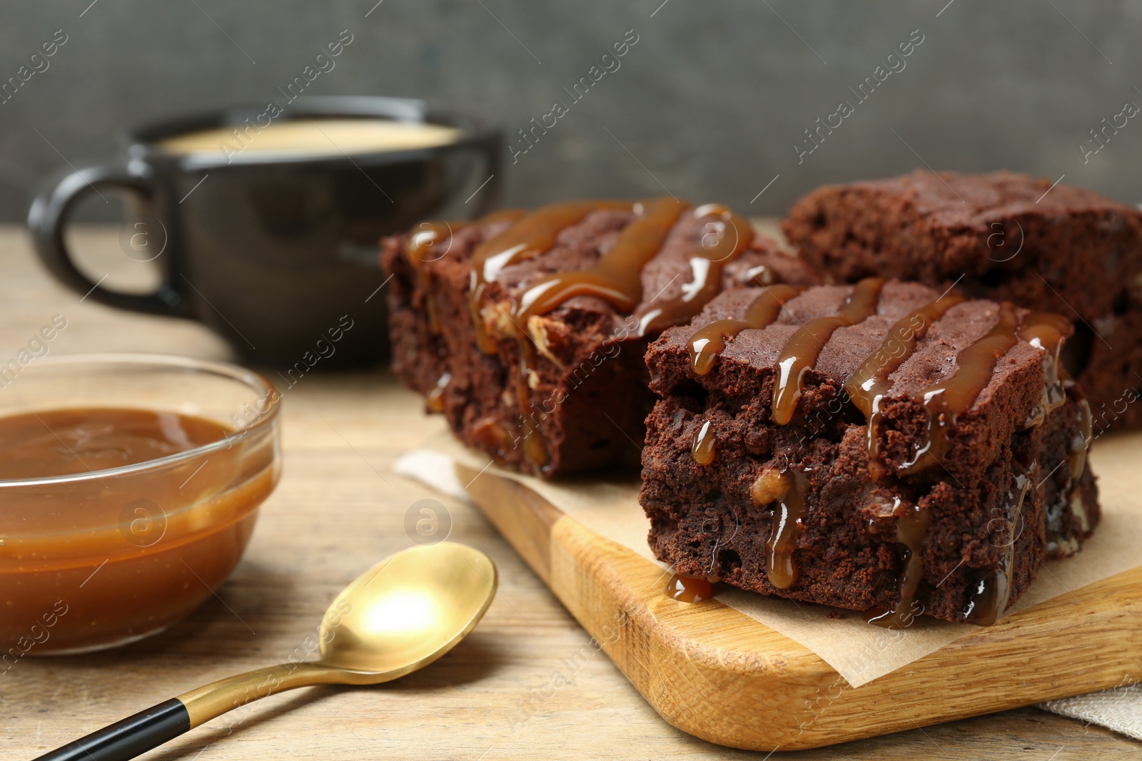 Photo of Delicious chocolate brownies with nuts and caramel sauce on wooden table