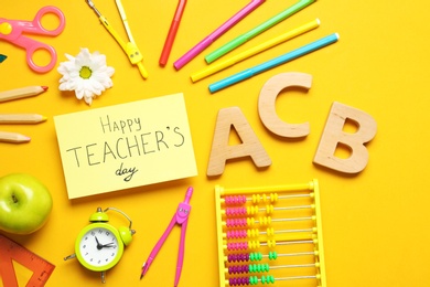 Photo of Flat lay composition of card with inscription HAPPY TEACHER'S DAY and stationery on orange background
