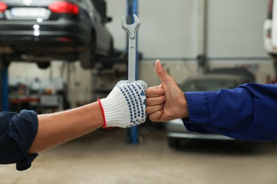 Photo of Mechanics making fist bump at automobile repair shop, closeup