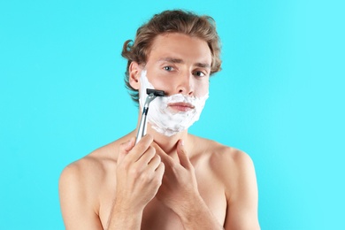 Photo of Handsome young man shaving on color background